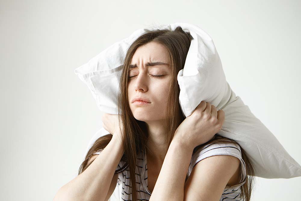 Krásná mladá žena v pruhovaném tričku nemůže usnout a v zoufalosti si drží polstář na hlavě